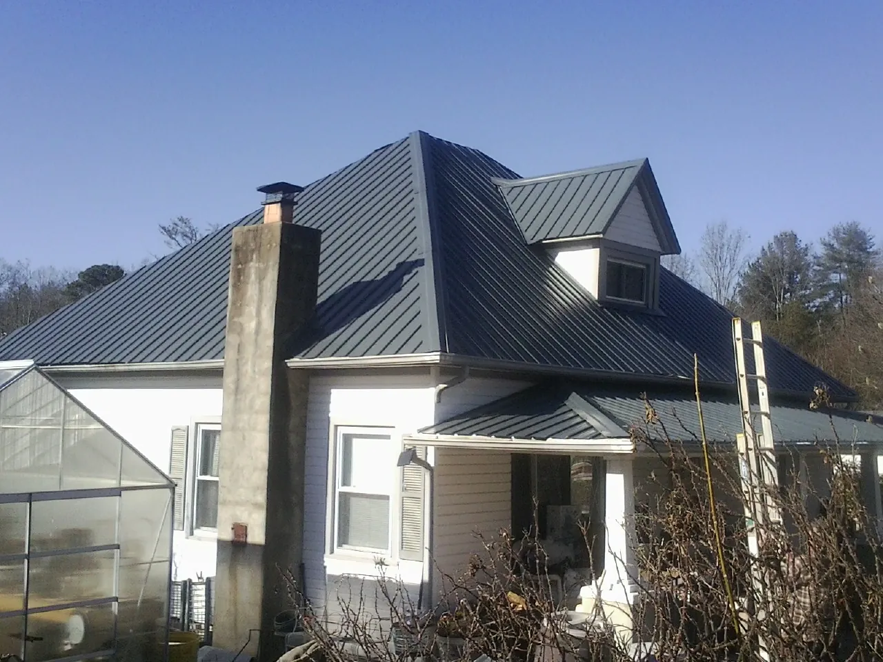 Dark blue standing seam metal roof on a white farmhouse with dormer — Slate & Tile Roof Repair by Roofing Brothers in Goodland