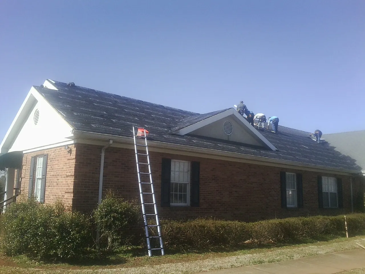 Crew tearing shingles off a brick ranch roof with a ladder set — Emergency Roof Repair work by our crew in Goodland