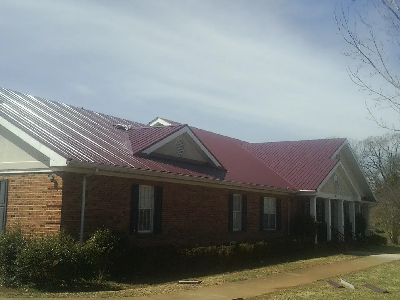Red metal roof with gabled entries on a long brick building, from a Hail Damage Roof Repair job in Goodland