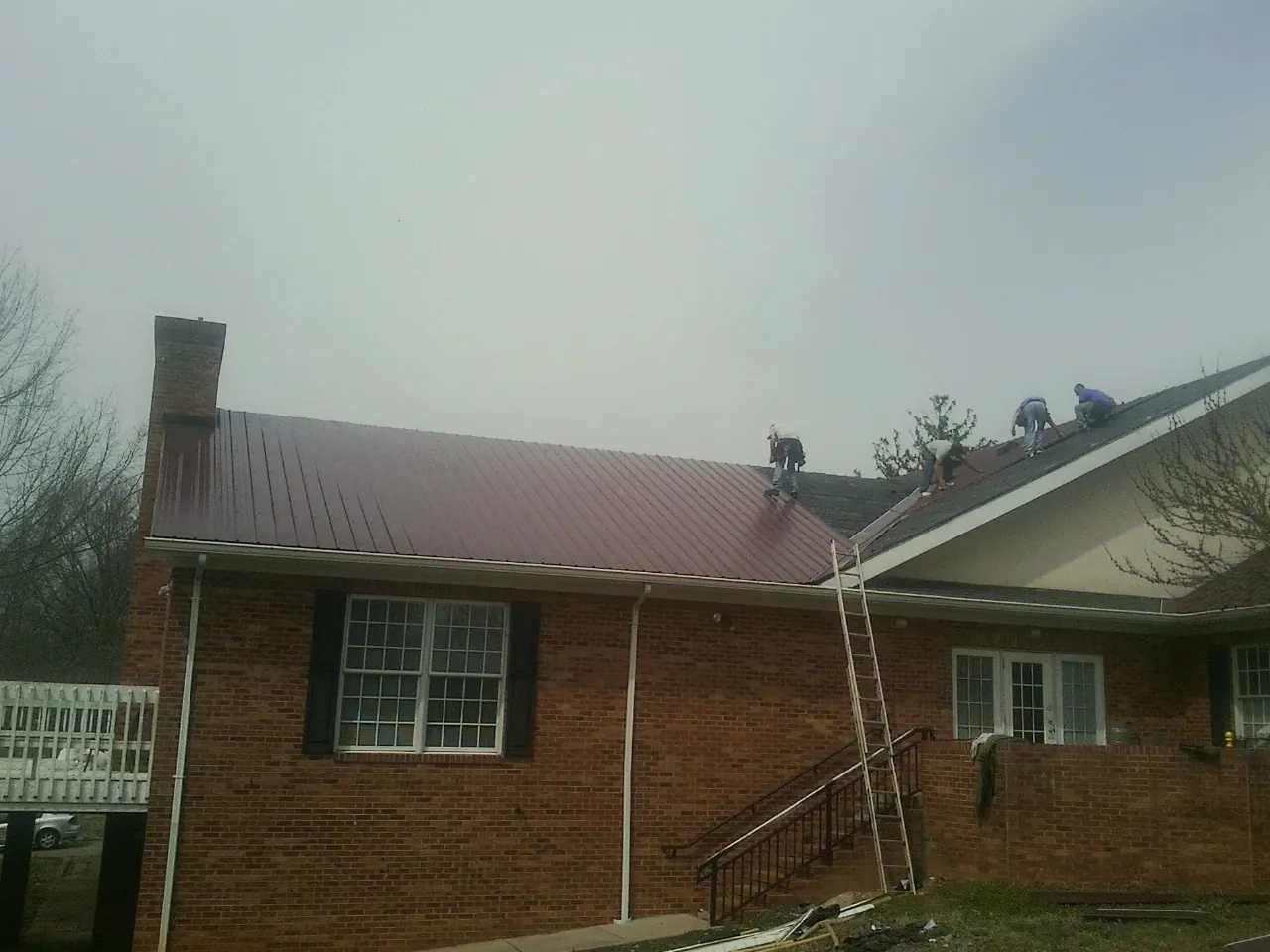 Crew setting red metal roofing panels on a brick home in Goodland
