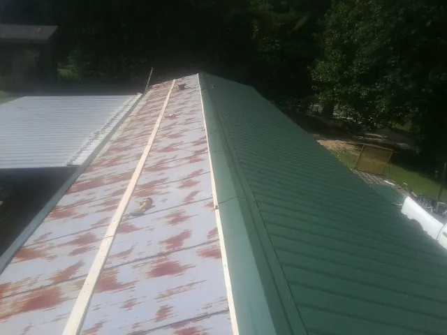 Old rusted panels beside newly installed green metal roofing — Wind Damage Roof Repair by Roofing Brothers in Goodland