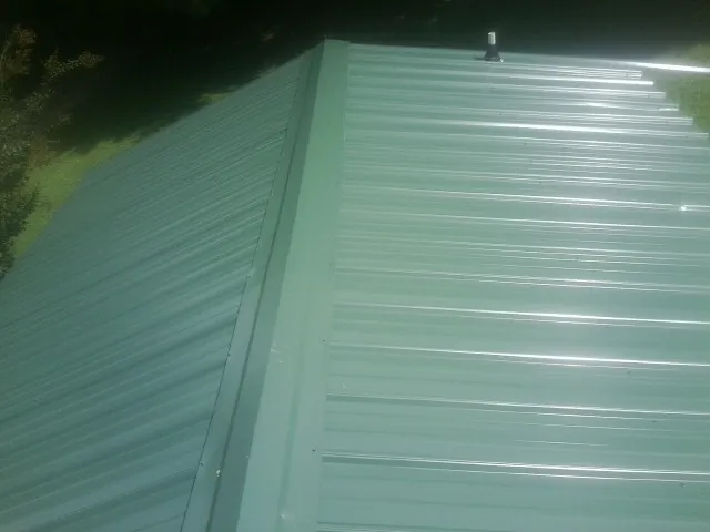 New green metal panels meeting at the ridge of a roof — Flat Roof Repair work by our crew in Goodland