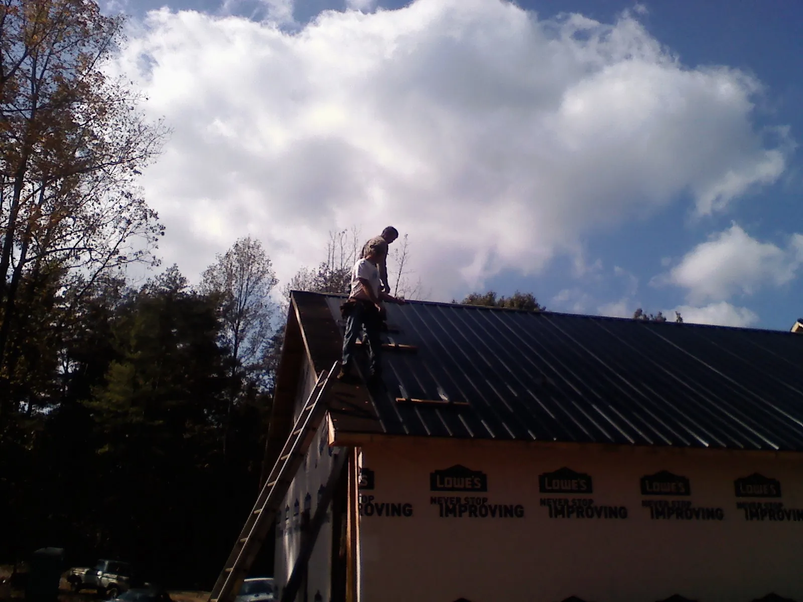 Roofer fastening dark metal panels high against a cloudy sky, from a Roof Inspection job in Goodland