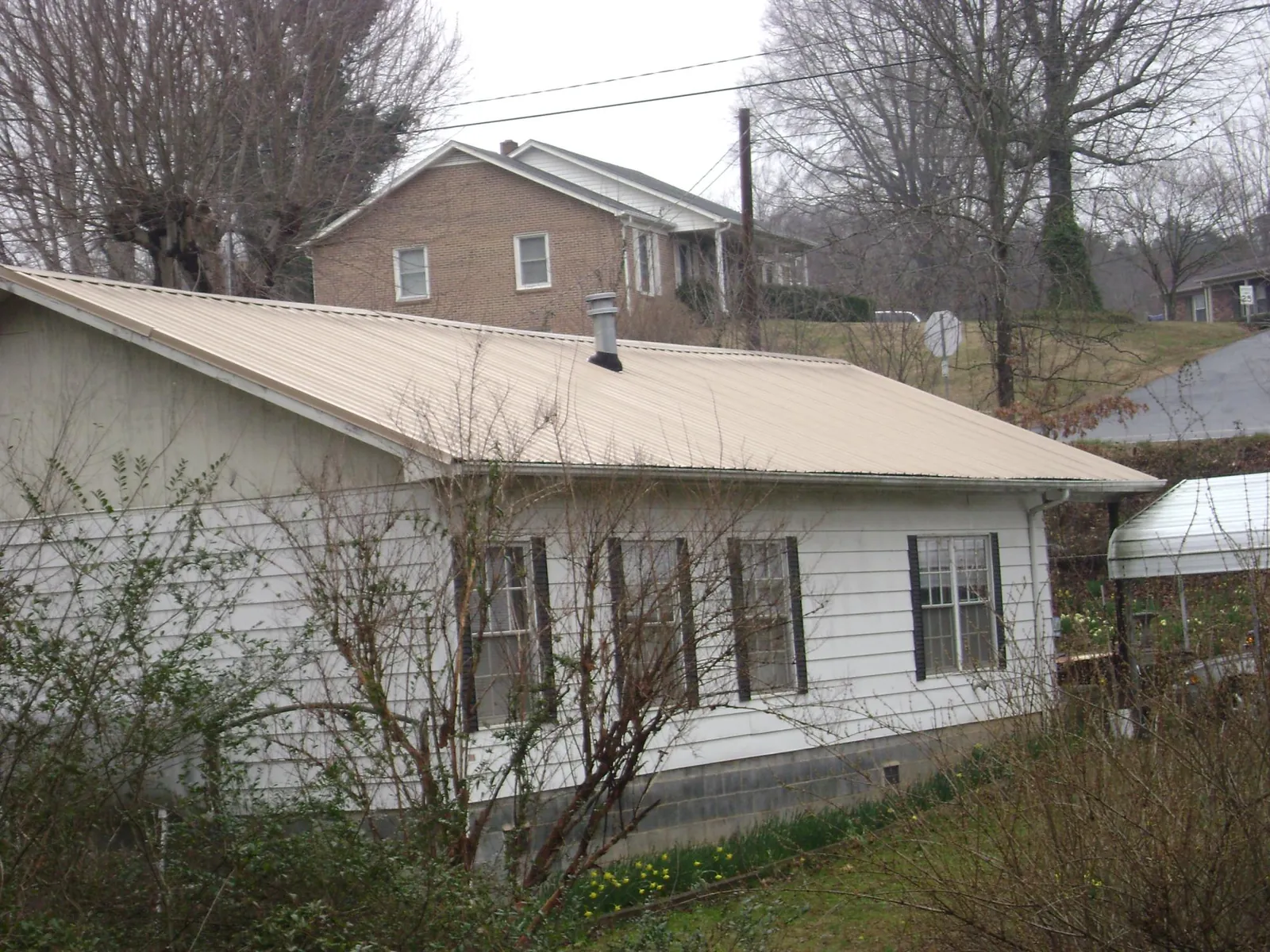 Tan metal roof on a white sided house set into a hillside — Commercial Roofing by Roofing Brothers in Goodland